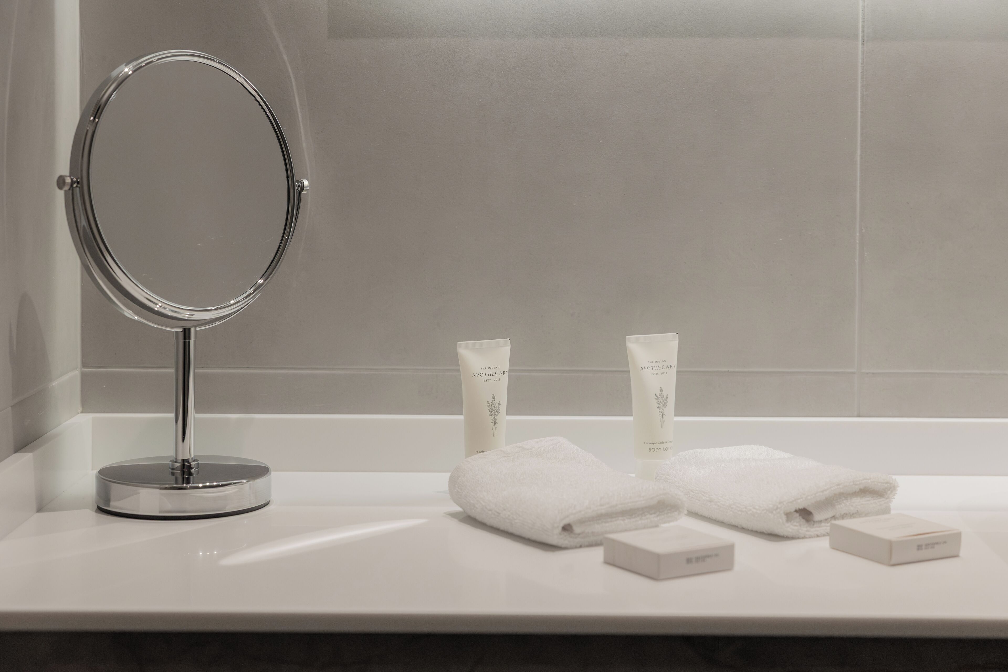 A bathroom vanity with a round mirror, two bottles of lotion, and two folded towels.