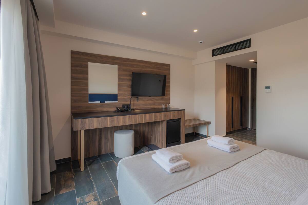 A hotel room with a bed, a desk, a mirror, a television, and a bathroom.