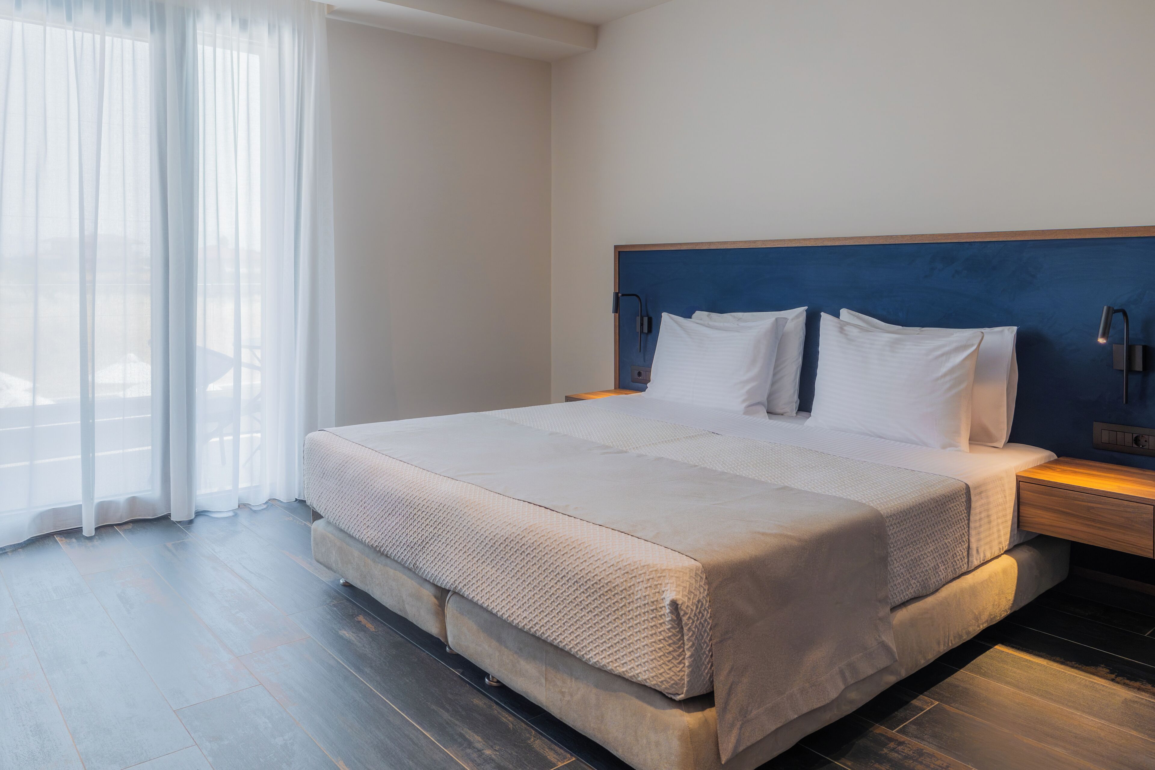 A modern hotel room with a large bed, a wooden headboard, and a nightstand with a lamp.