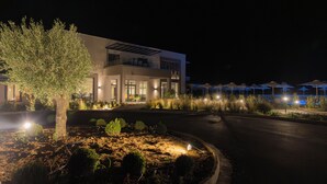 Un hotel moderno con un jardín ajardinado, un camino de entrada curvo y sombrillas exteriores.