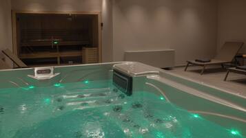 A modern spa area with a hot tub, lounge chairs, and a wooden sauna.