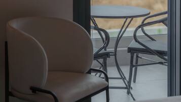 A room with a bed, a chair, and a table with a view of a field and mountains.