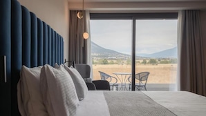 Habitación de hotel con una cama grande, vistas al campo y un balcón con sillas.