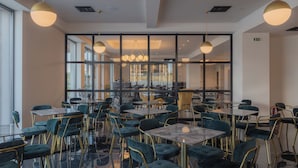 Un comedor moderno con mesas y sillas, ventanas amplias e iluminación colgante.