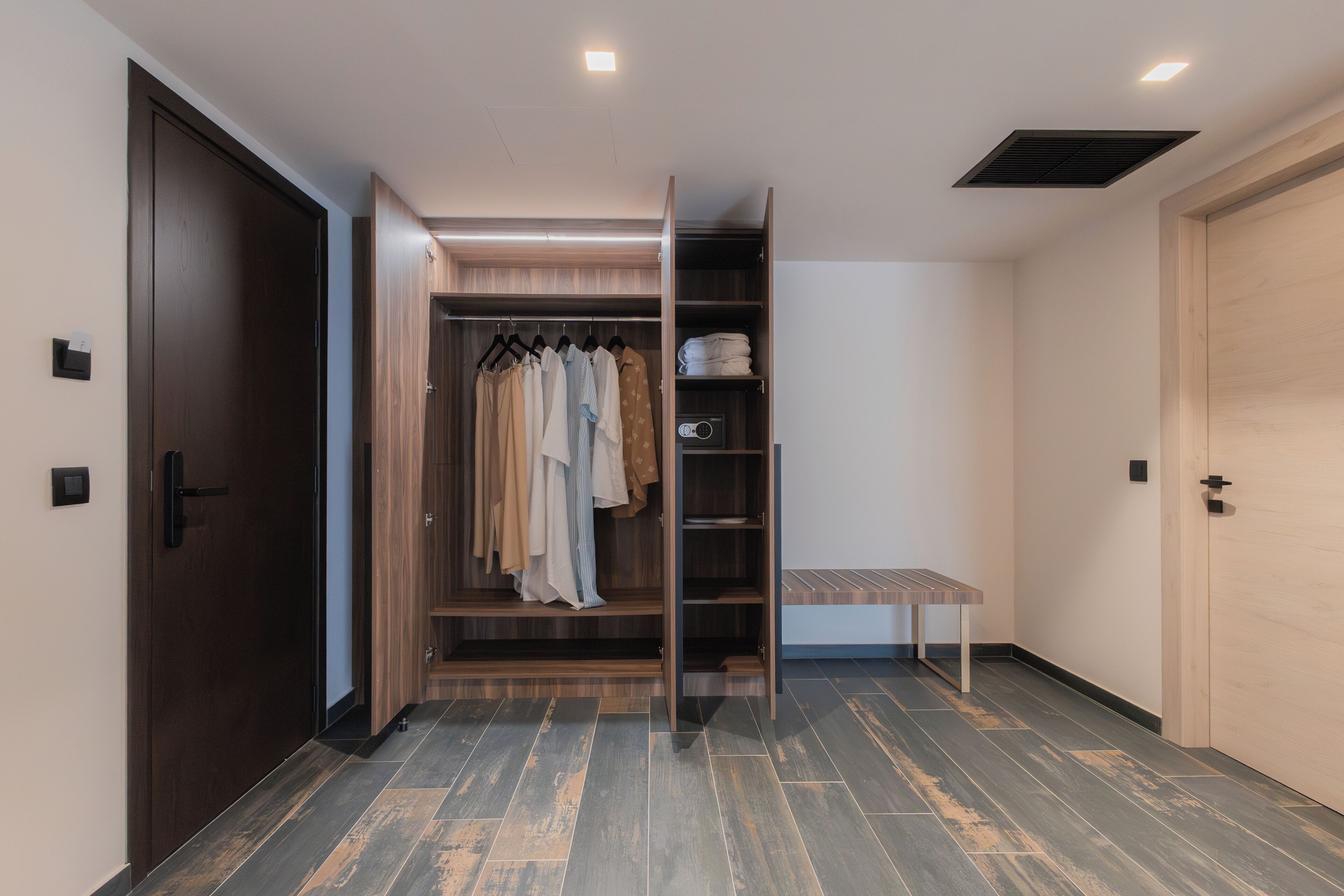 Um closet espaçoso com roupas penduradas, prateleiras e um banquinho.