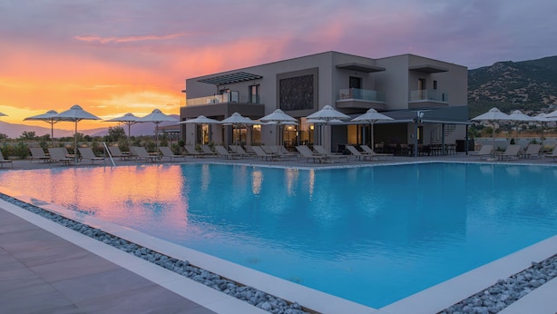 Un hotel moderno con piscina, tumbonas y sombrillas.