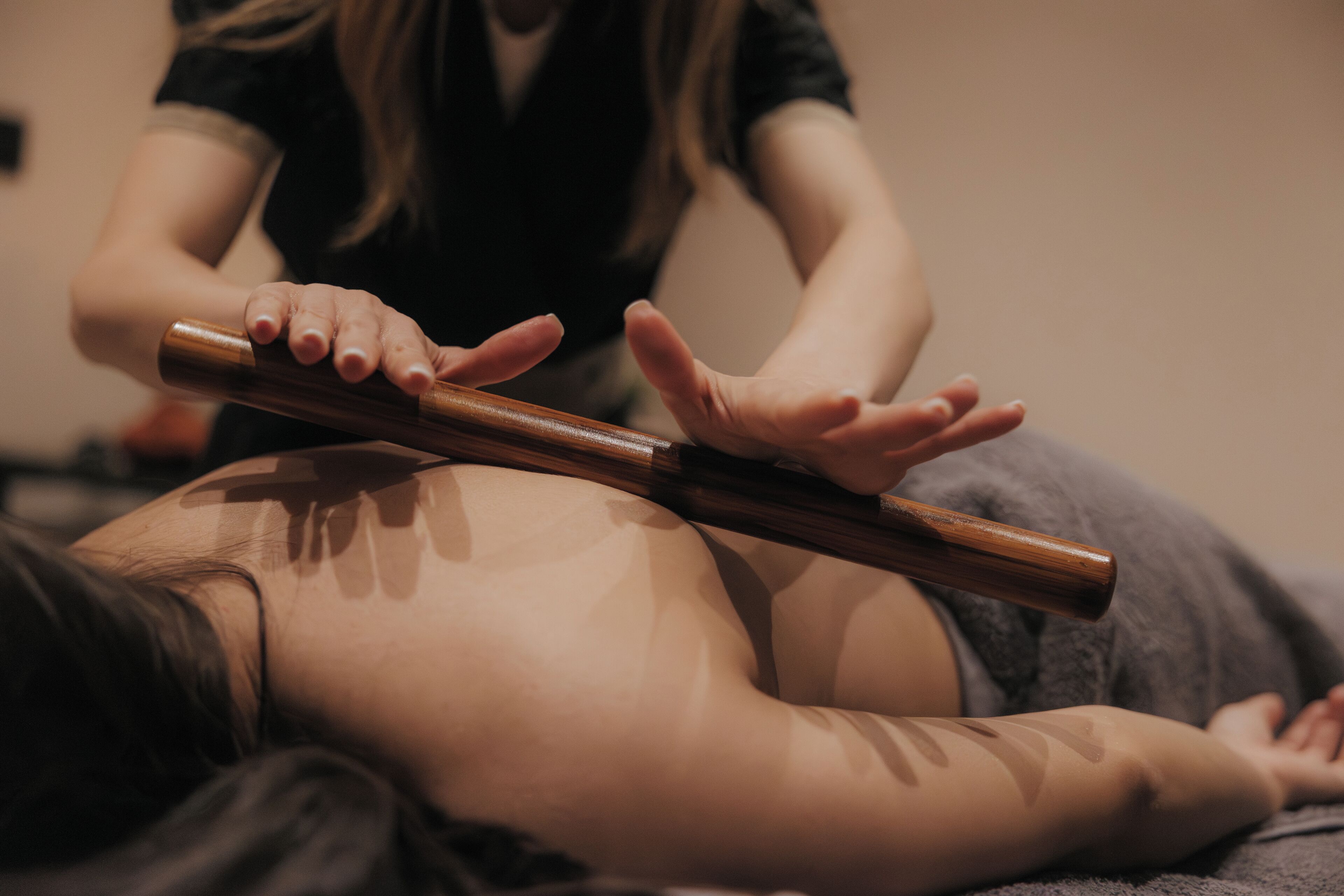 A person lying on a massage table receiving a back massage with a wooden tool.