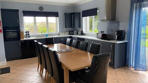 A modern kitchen with a dining area, featuring a large island, dark cabinetry, and a view of the outdoors. - Ballygarrett Holiday Home (Cahore)