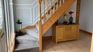 A staircase with wooden balusters, a small side table with a plant, and a cabinet with drawers. - Ballygarrett Holiday Home (Cahore)