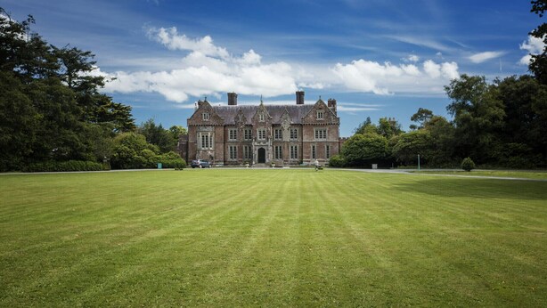A large, historic building with a symmetrical facade, surrounded by a well-maintained lawn and dense trees. - Ballygarrett Holiday Home (Cahore)