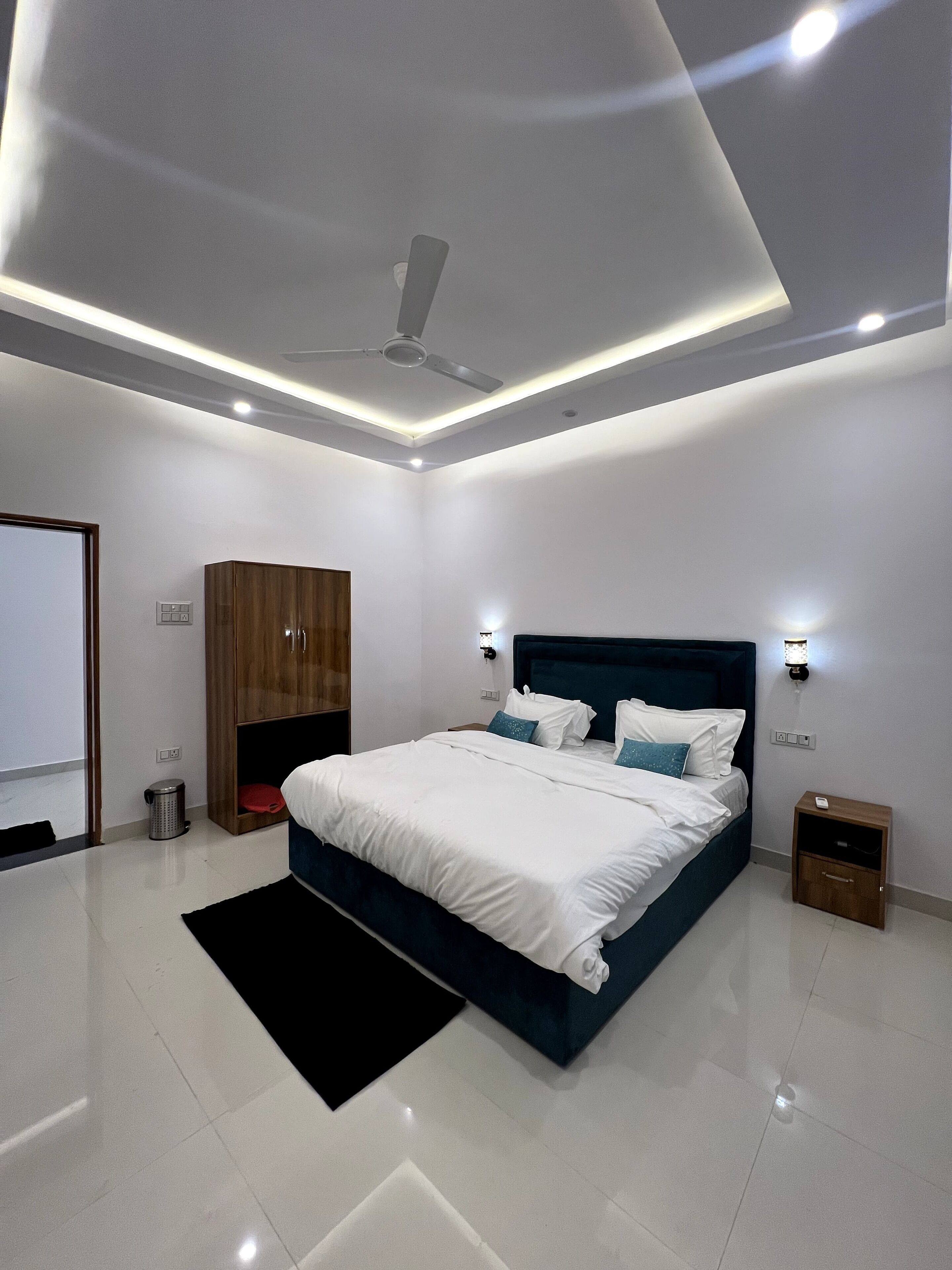 A modern bedroom with a large bed, a ceiling fan, recessed lighting, a wardrobe, and a nightstand.