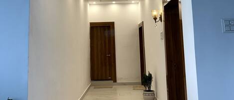 Un pasillo moderno con una puerta de madera al final, iluminación empotrada y una planta en maceta.