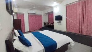 A hotel room with a large bed, a flat-screen TV mounted on the wall, and pink curtains. - Hotel Atithi Mount Abu (Mount Abu)