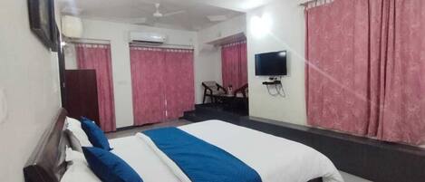 A hotel room with a large bed, a flat-screen TV mounted on the wall, and pink curtains.