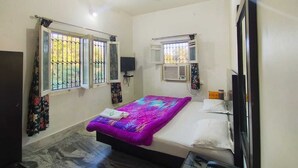 A bedroom with a bed, a ceiling fan, a TV, and a window with a view of greenery. - Hotel Atithi Mount Abu (Mount Abu)