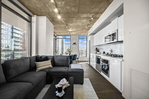Um apartamento moderno com sofá seccional cinza, mesa de jantar e cozinha com armários brancos e eletrodomésticos de aço inoxidável.