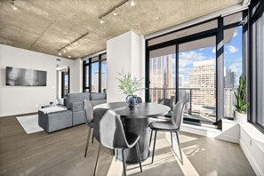 Um interior moderno com área de refeições, um sofá cinzento e janelas amplas com vista para a cidade.