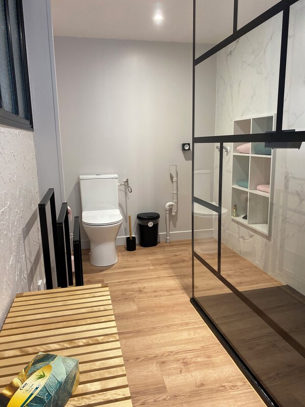Une salle de bain moderne équipée de toilettes, d’un bidet et d’une cloison en verre avec des étagères.