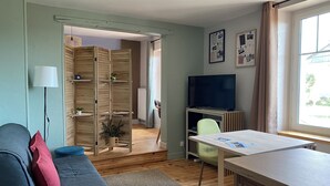 A compact living space with a sofa, a dining table, a TV, and a wooden wardrobe. - Gîte PREY DES VOSGES (Prey)