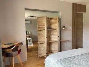 Une chambre comprenant un lit, un bureau avec une chaise, une armoire et une petite plante posée sur une étagère.