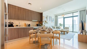 A modern living room with a dining area, a kitchen with wooden cabinets, and large windows offering a city view. - Beach Vista Residences - Dubai Harbour (Dubai)