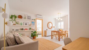 A modern living room with a sofa, a dining table, and a kitchen area in the background. - Casa Flor do Mar - Beautiful apt in the centre of Carvoeiro (Carvoeiro)