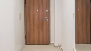 Een houten deur met een deurklink en slot, een lichtschakelaar en een kleine spiegel aan de muur.
