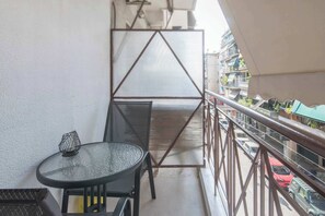 A balcony with a glass table and chairs, a metal screen, and a view of parked cars and buildings.