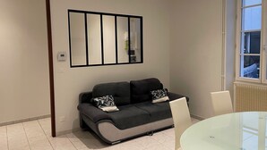 A modern living room with a sofa, a glass table, and a large window. - Logis du 96 (Angoulême)
