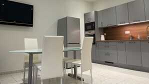 A modern kitchen with grey cabinets, a built-in oven, a microwave, and a flat-screen TV mounted on the wall. - Logis du 96 (Angoulême)
