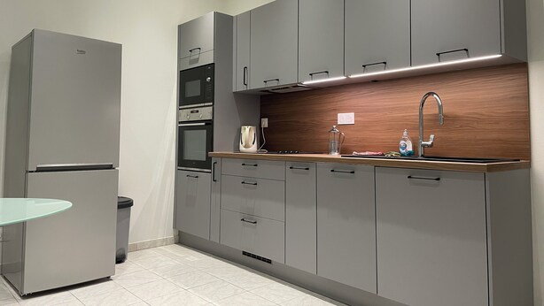 A modern kitchen with grey cabinets, a stainless steel refrigerator, a built-in oven, and a wooden countertop. - Logis du 96 (Angoulême)