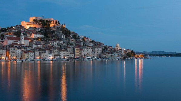 A coastal town with historic buildings, a prominent castle on a hill, and a calm harbor with boats.