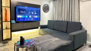 Ein modernes Wohnzimmer mit Fernseher, einer Couch, einem Couchtisch, einer Uhr und einem dekorativen Regal.