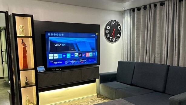 Ein modernes Wohnzimmer mit Fernseher, einer Uhr, einer Couch und einem dekorativen Glastisch.