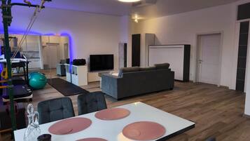 A spacious living room with a grey sofa, a TV, and exercise equipment.