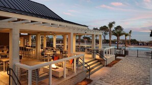 An outdoor dining area with tables and chairs, a pool, and palm trees. - Ocean Oak by Hilton Grand Vacations: Your 2-Bedroom Coastal Haven (Hilton Head Island)