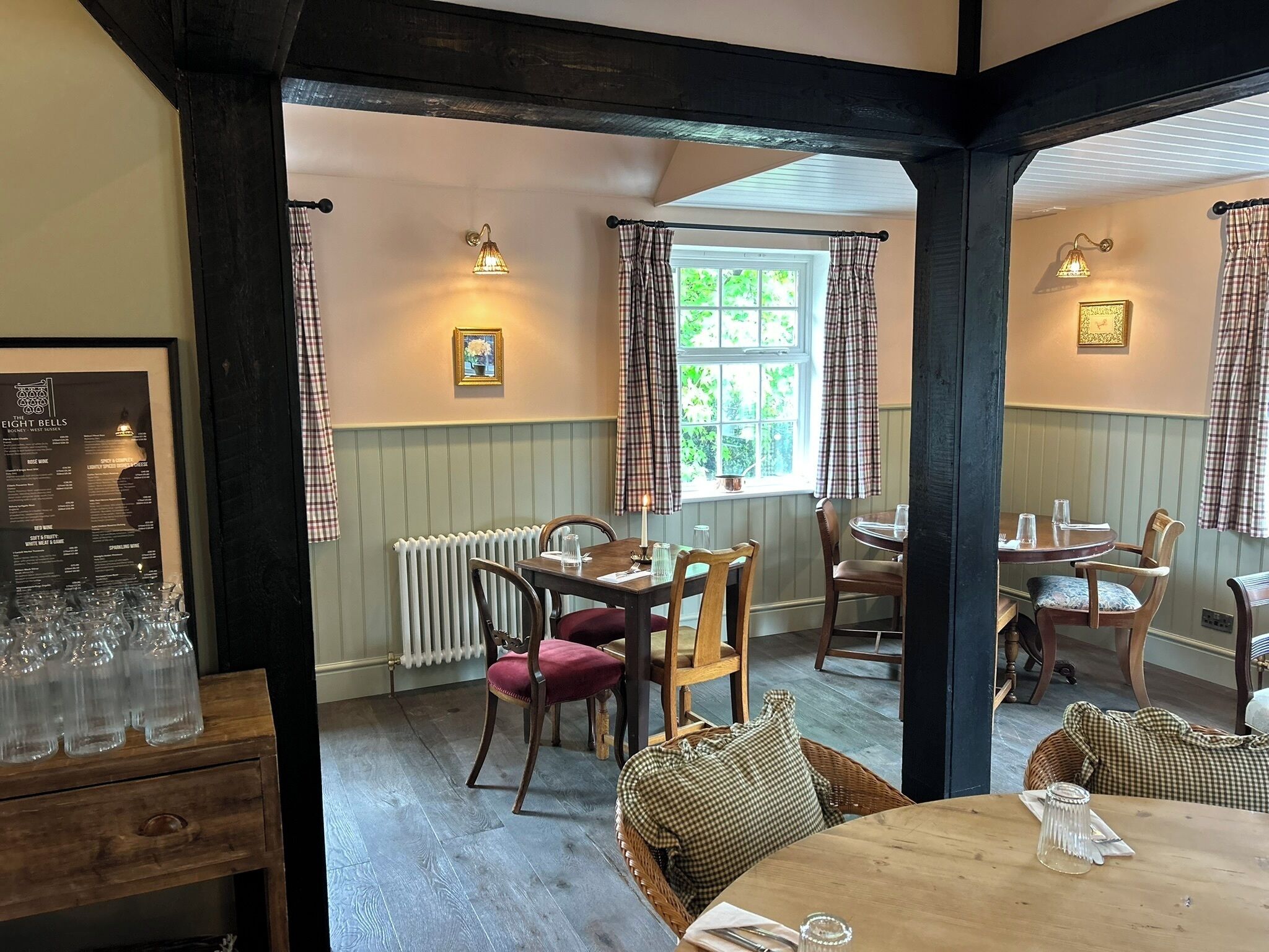 Un comedor acogedor con mesas y sillas de madera, un menú enmarcado en la pared y una ventana con cortinas.