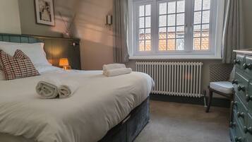 Cama bem arrumada com toalhas dobradas, abajur, radiador e uma cadeira com almofada.