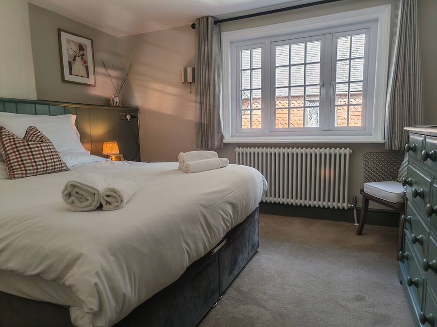 Cama bem arrumada com toalhas dobradas, abajur, radiador e uma cadeira com almofada.