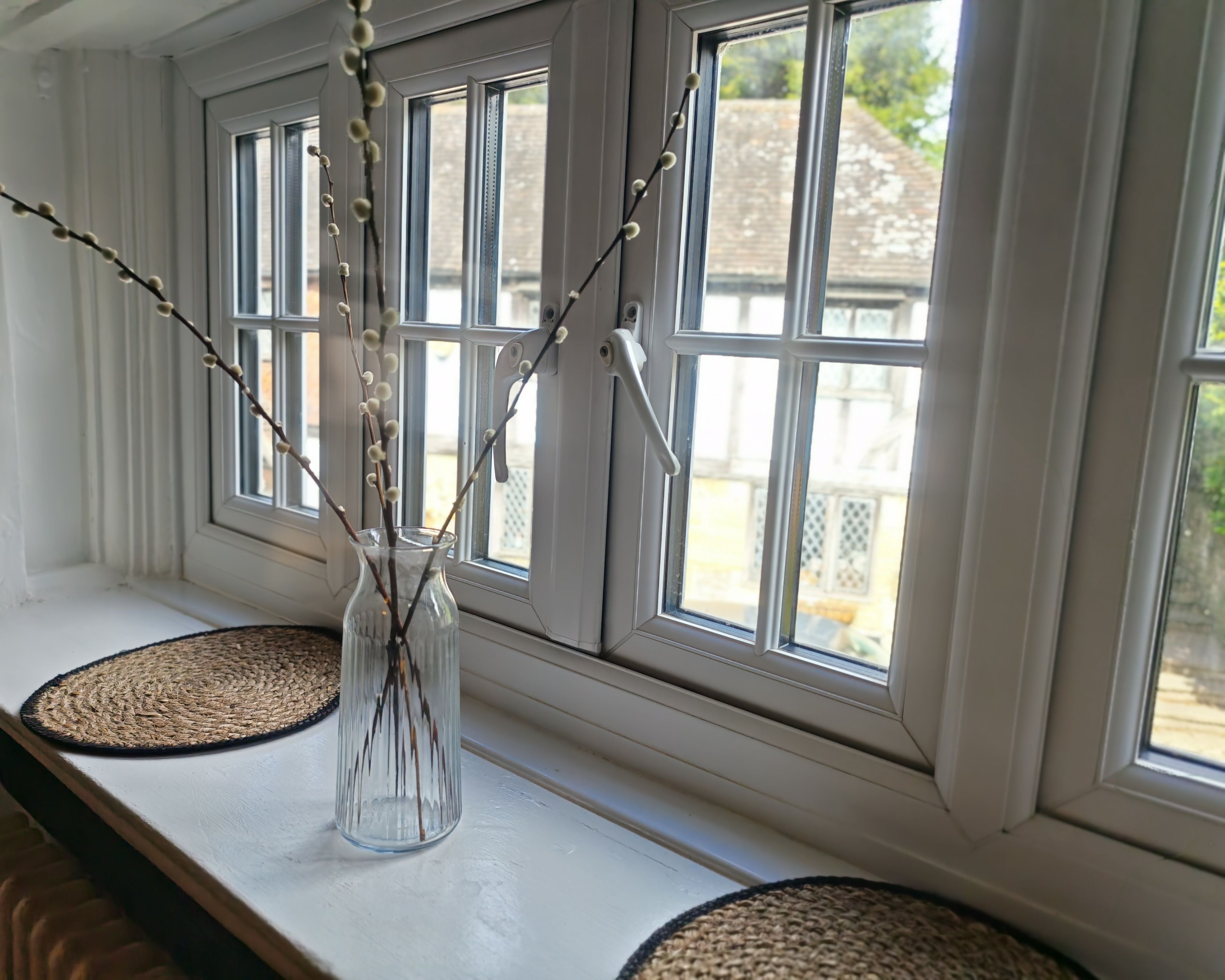 A window with a clear view of the outside, a vase with branches, and two woven mats on the sill.