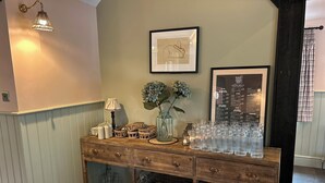 A wooden console table with glassware, baskets, and a vase with flowers. - The Eight Bells Inn (Bolney)