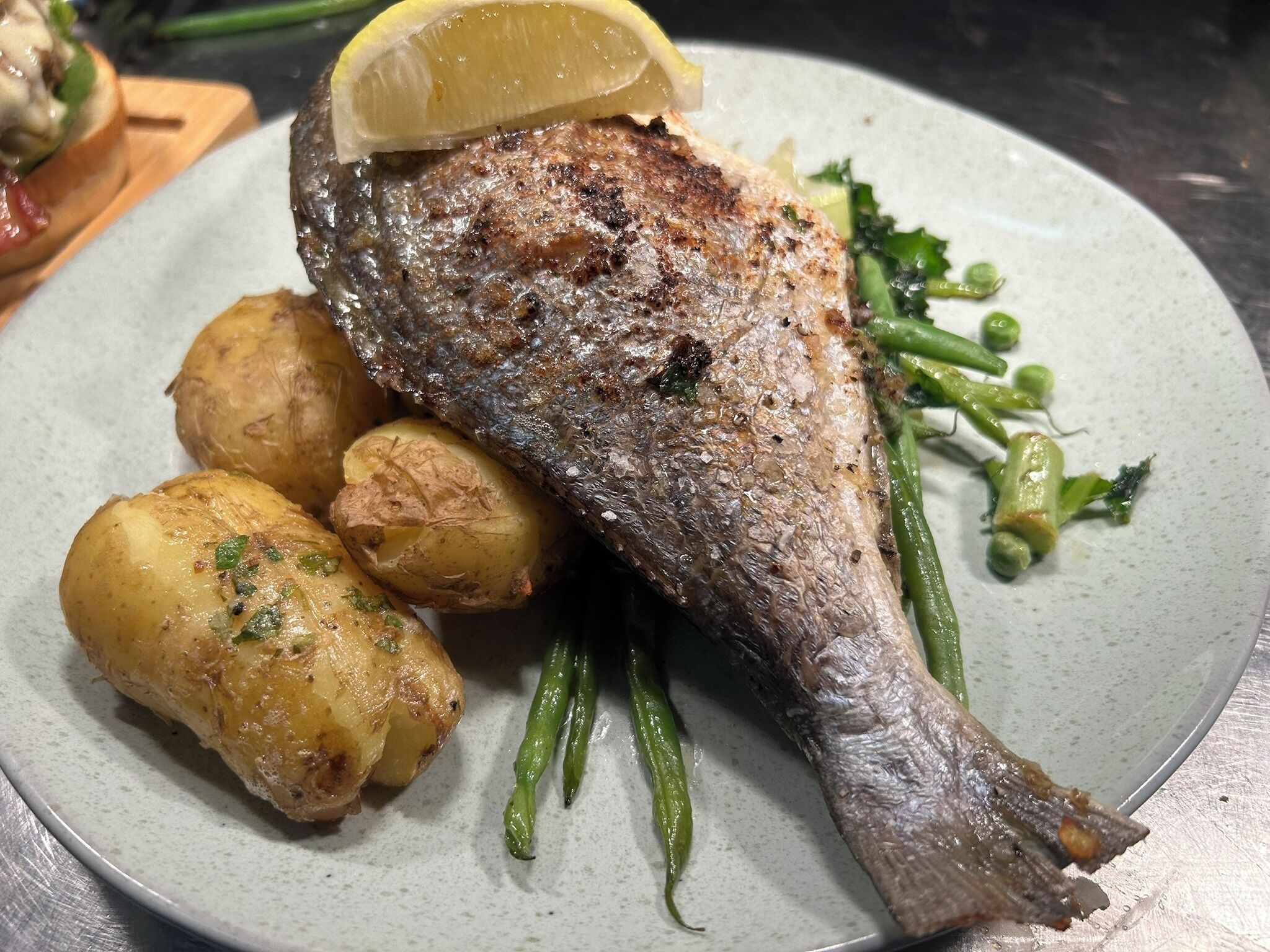 A plate with a grilled fish, roasted potatoes, and green beans.