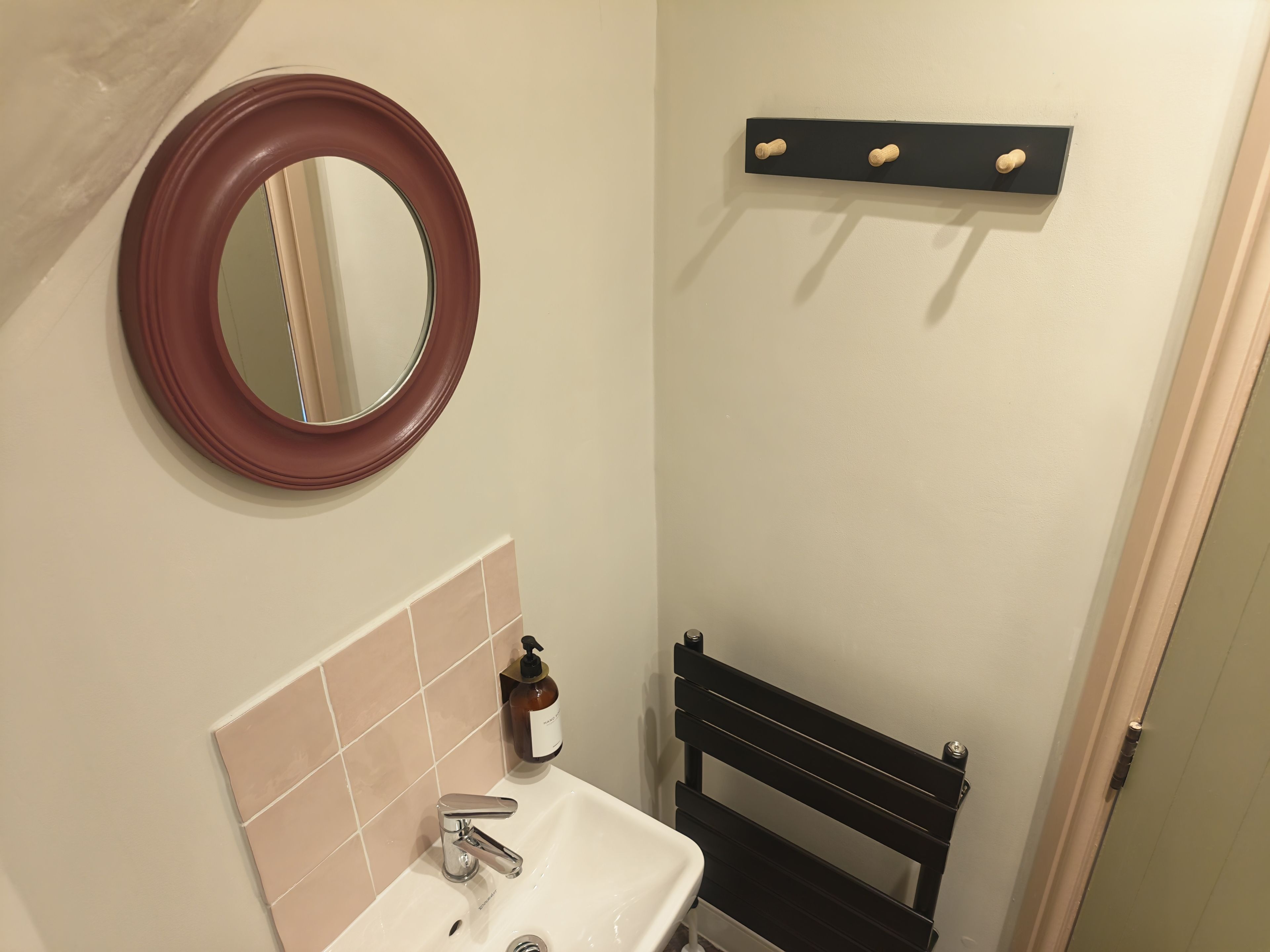 A bathroom with a round mirror, a sink, a soap dispenser, and a black bench.