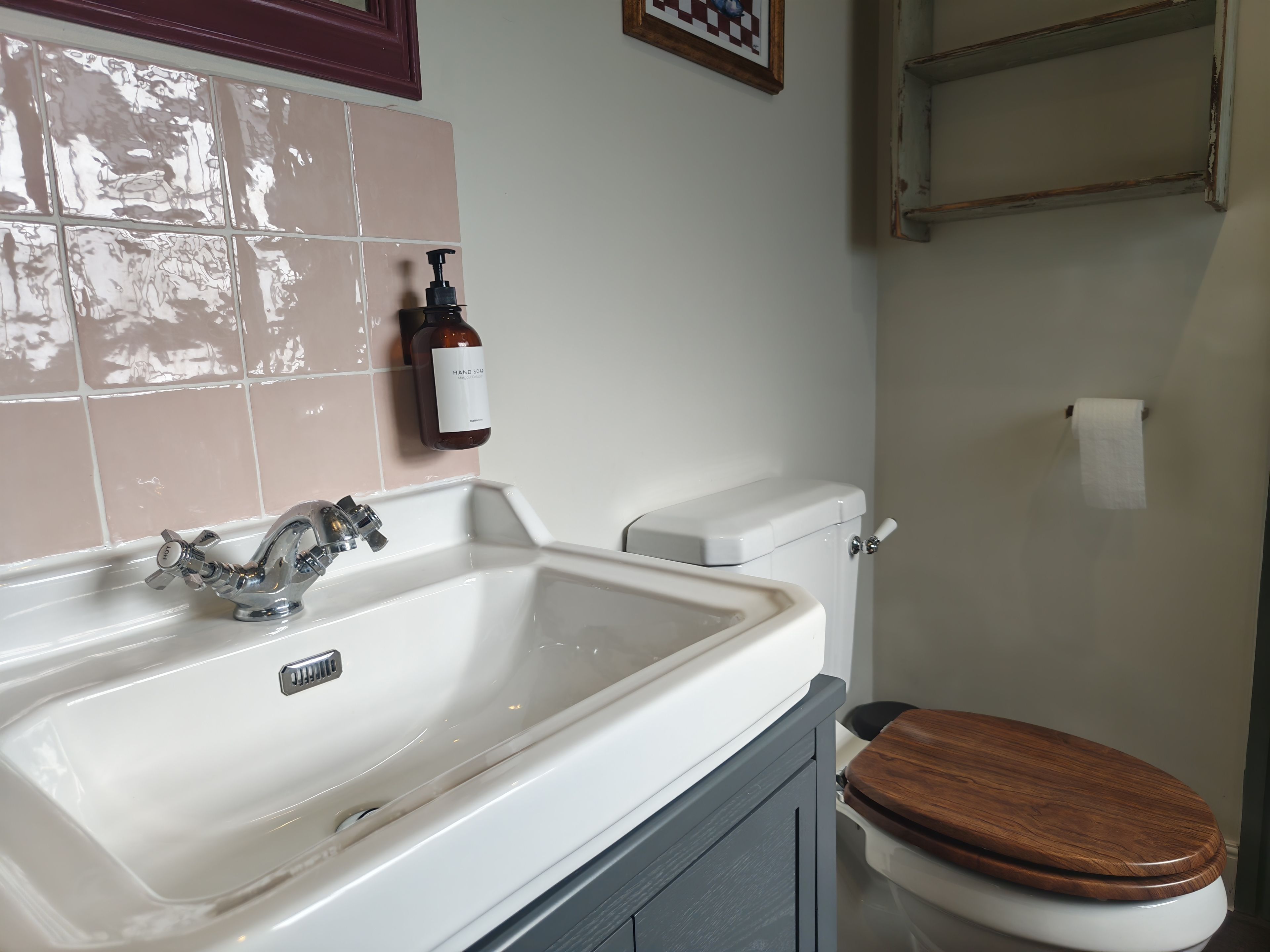 A bathroom with a white sink, a wooden toilet seat, and a bottle of hand soap on the wall.
