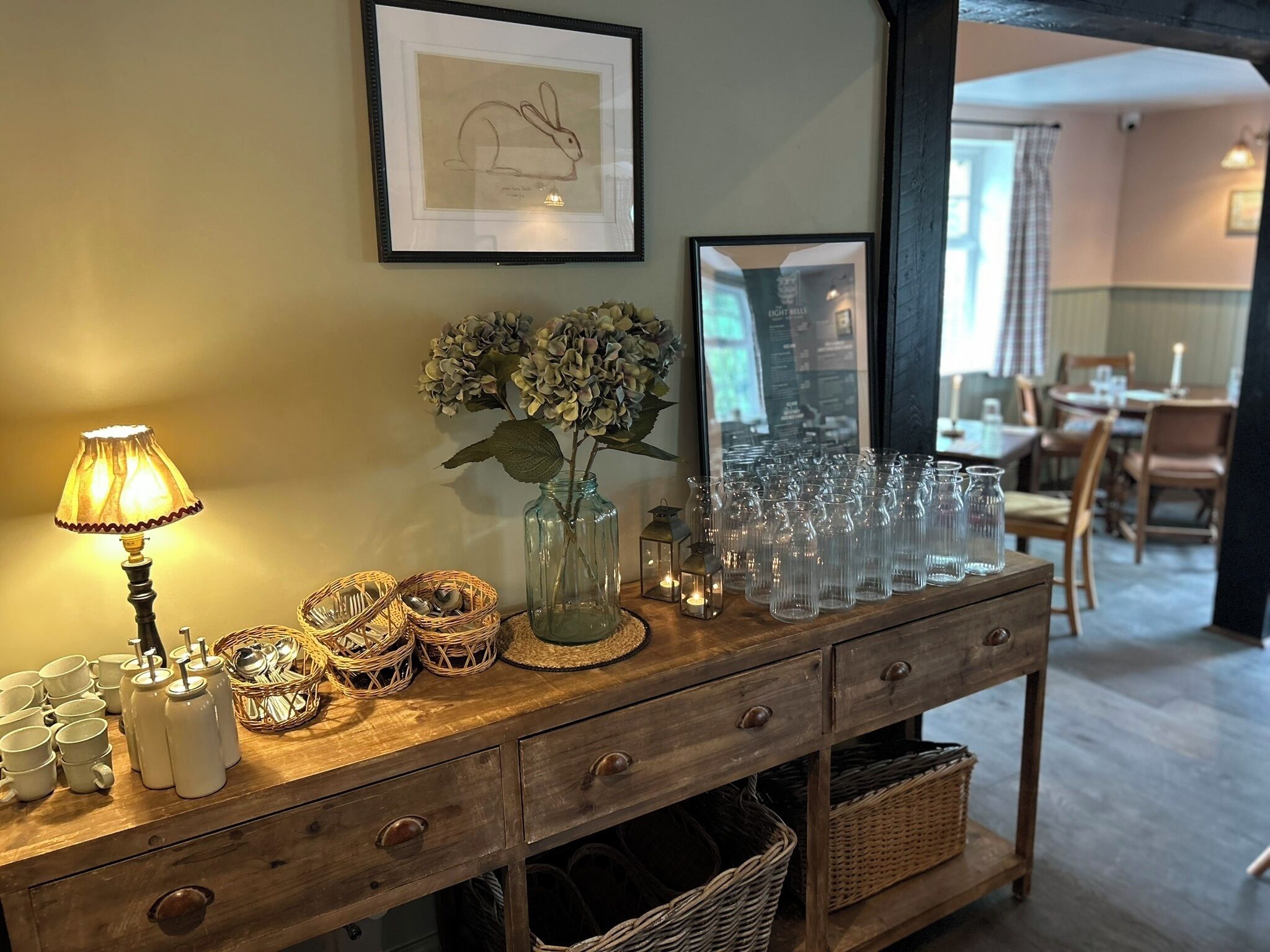 A wooden console table with a lamp, glassware, and wicker baskets.