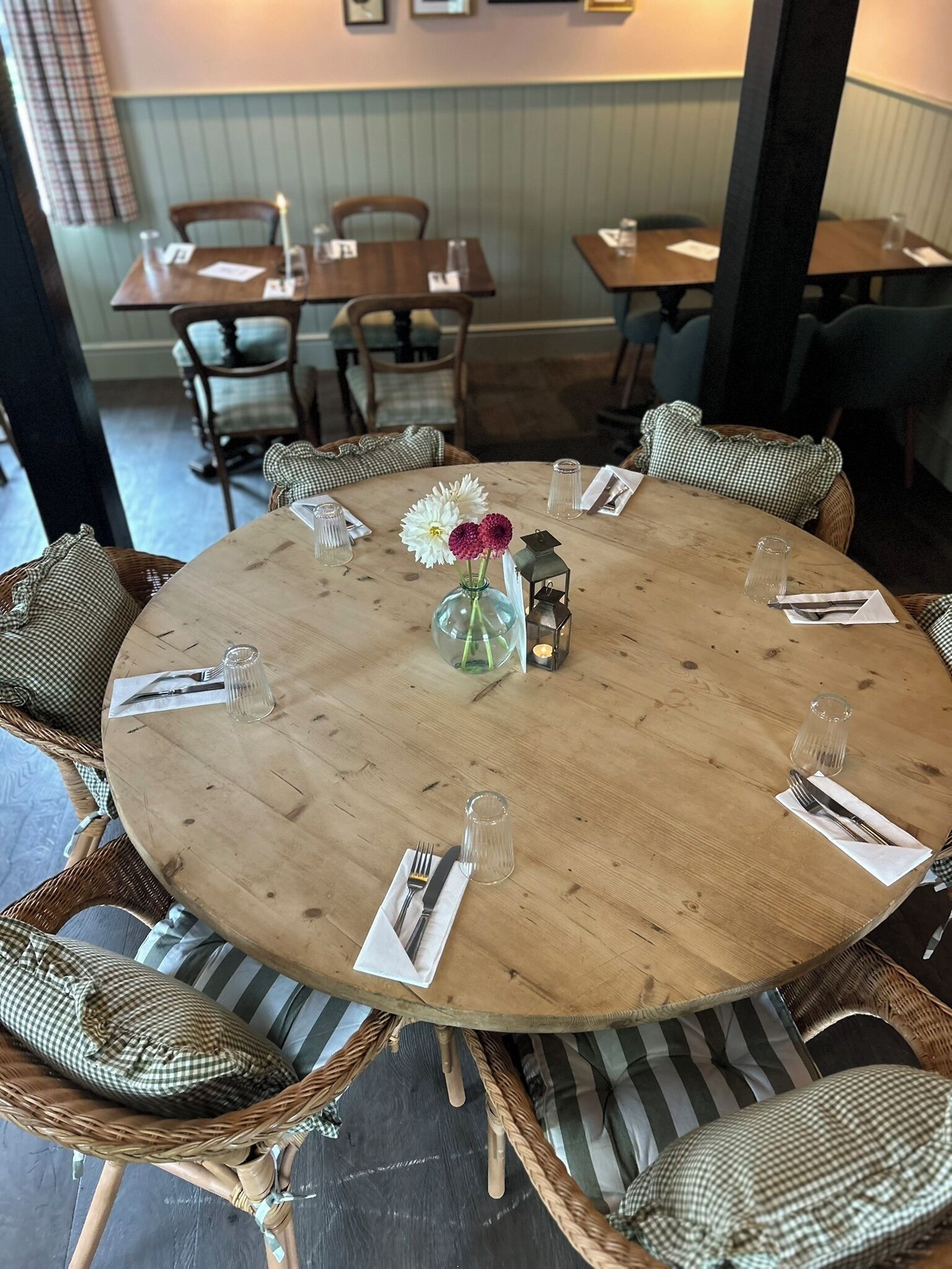 A round wooden table with a vase of flowers, surrounded by wicker chairs with striped cushions.