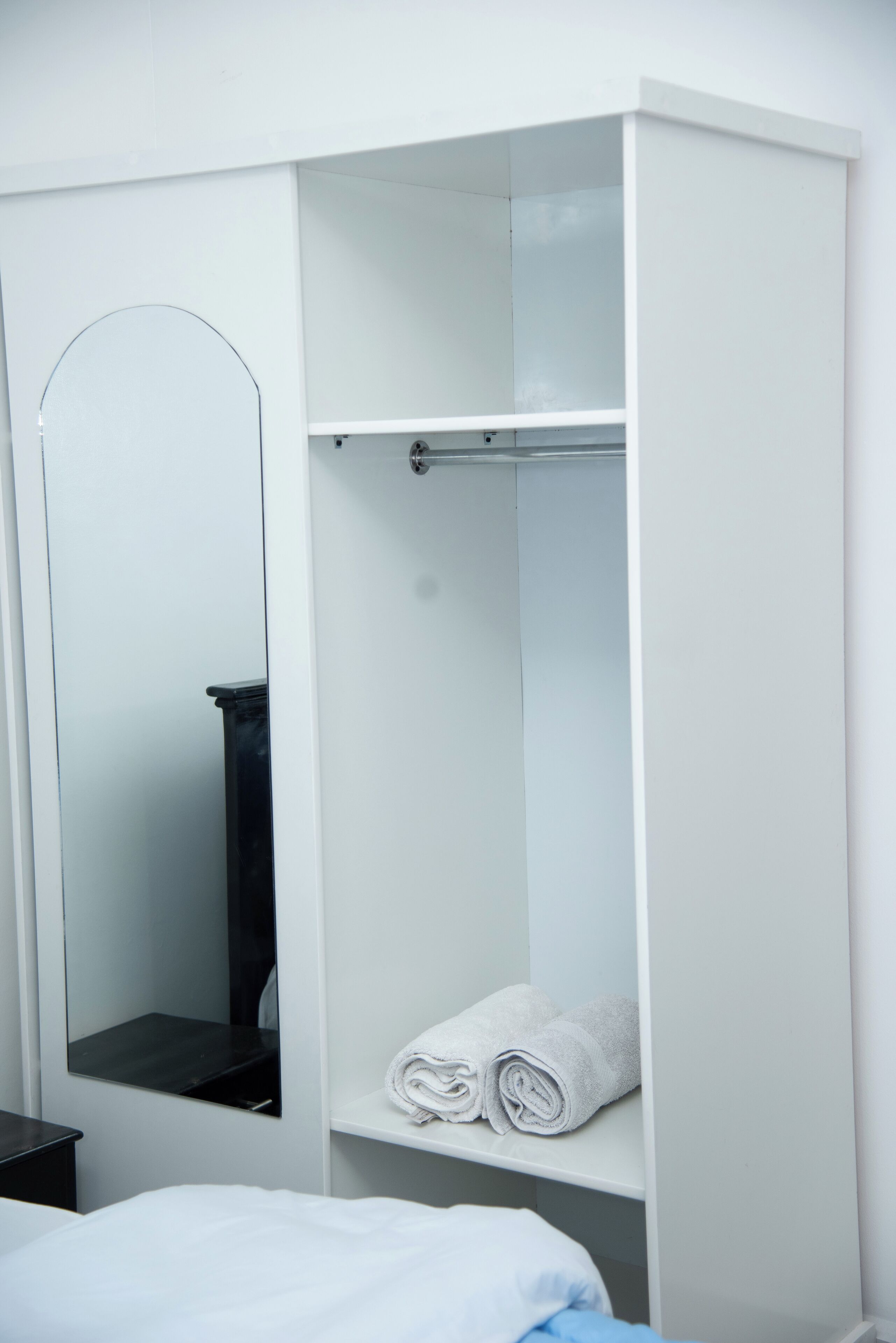 Um guarda-roupa branco com espelho, uma prateleira com toalhas dobradas e uma cama com roupa de cama branca.