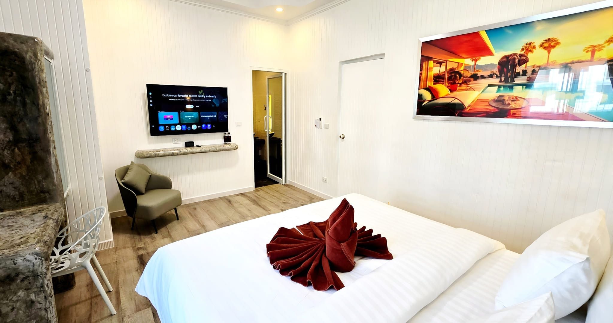 A hotel room with a bed, a TV mounted on the wall, a painting, and a wooden floor.