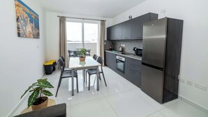 A modern kitchen with a large refrigerator, dark cabinets, and a dining area with a table and chairs.