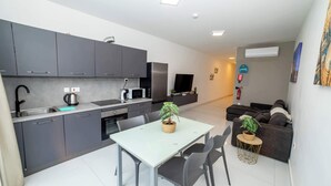 A modern kitchen with grey cabinets, a dining table with chairs, a small round table with a plant, and a grey sofa in the living area.